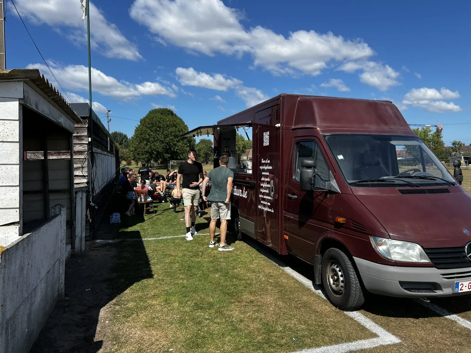 De bordeaux foodtruck van Huurjefrituur op een zonnig feest naast een sportterrein